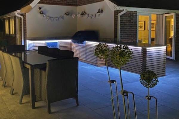 Nighttime photo of an outdoor kitchen with lighting underneath it.