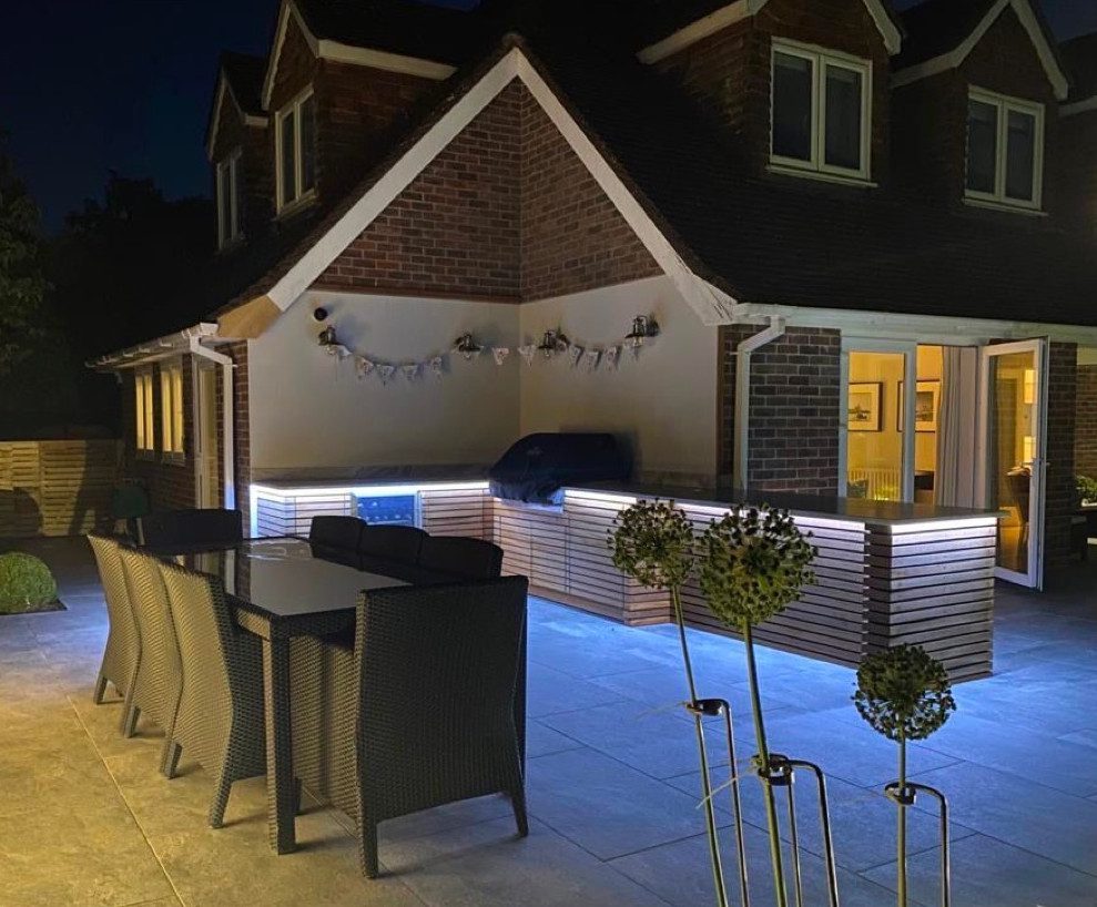 A nighttime photo taken of a bespoke outdoor kitchen with neon lights underneath.